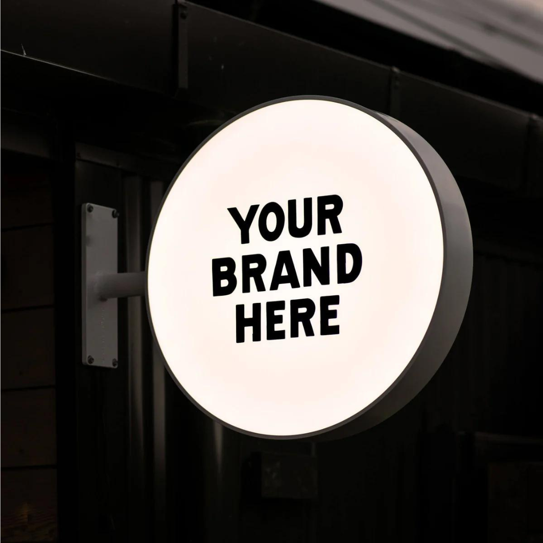 Illuminated lightbox sign mounted on a shopfront, designed to attract attention day and night.