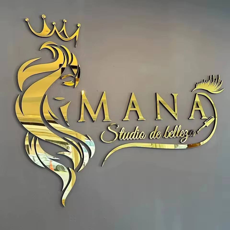 Gold mirror acrylic logo with a crown, a woman's profile, MANA lettering and script tagline on a grey wall