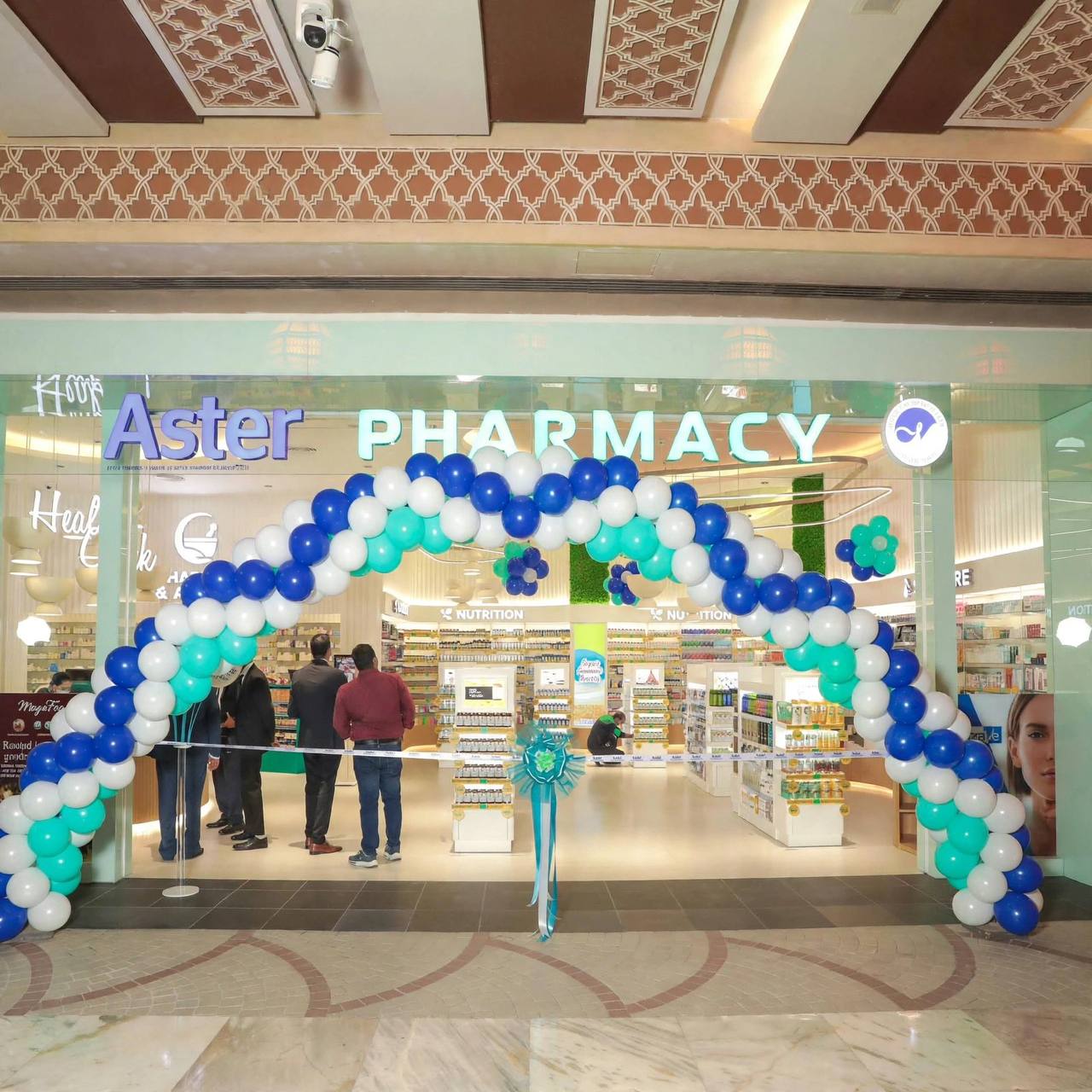 Aster Pharmacy entrance with illuminated 3D letters and a balloon arch