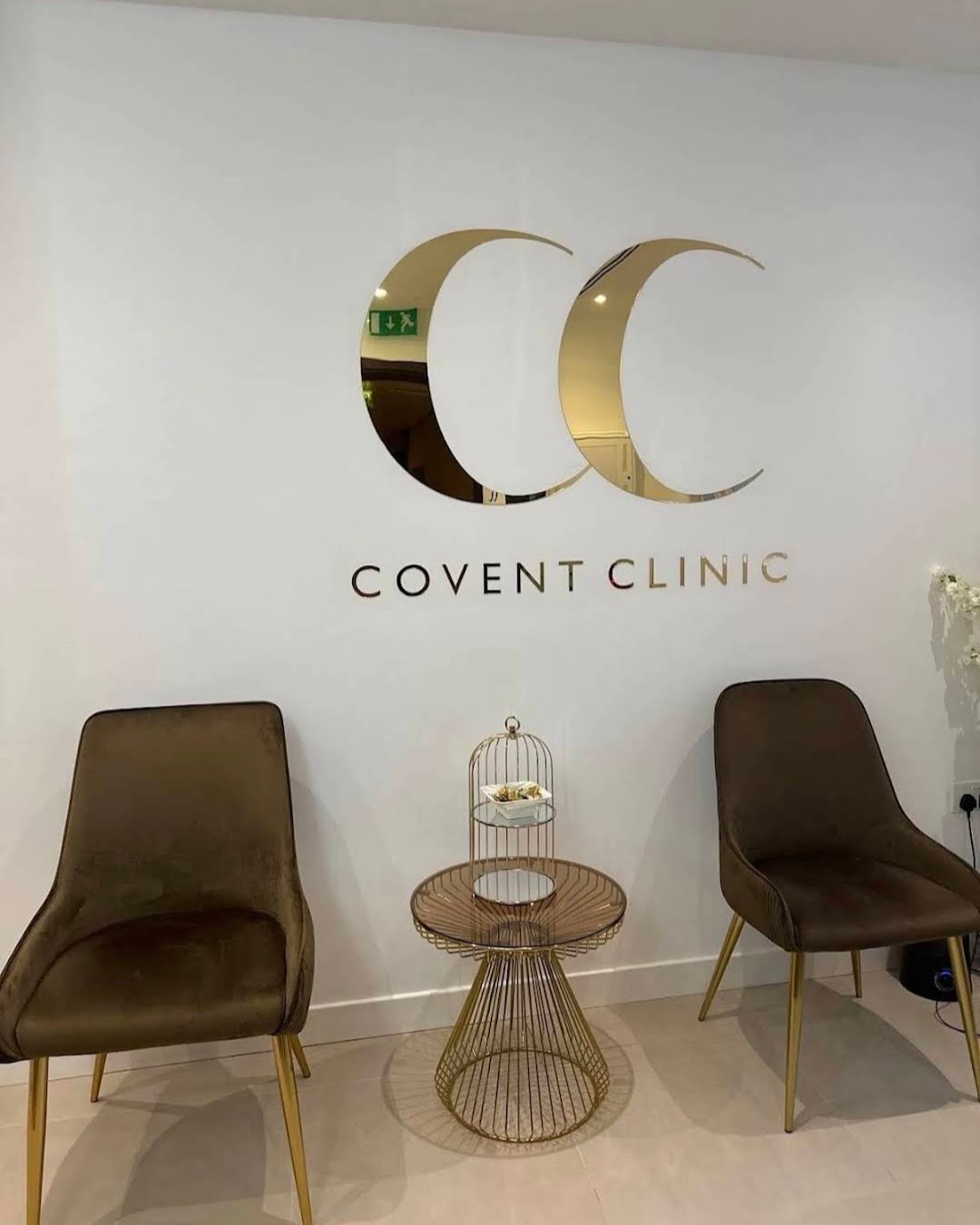 Mirror gold CC logo with COVENT CLINIC lettering above two chairs and a gold side table